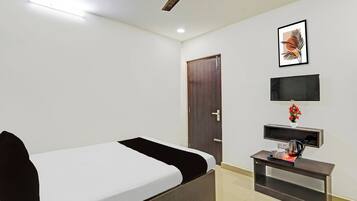 A hotel room with a bed, a desk with a telephone, a television, and a door.