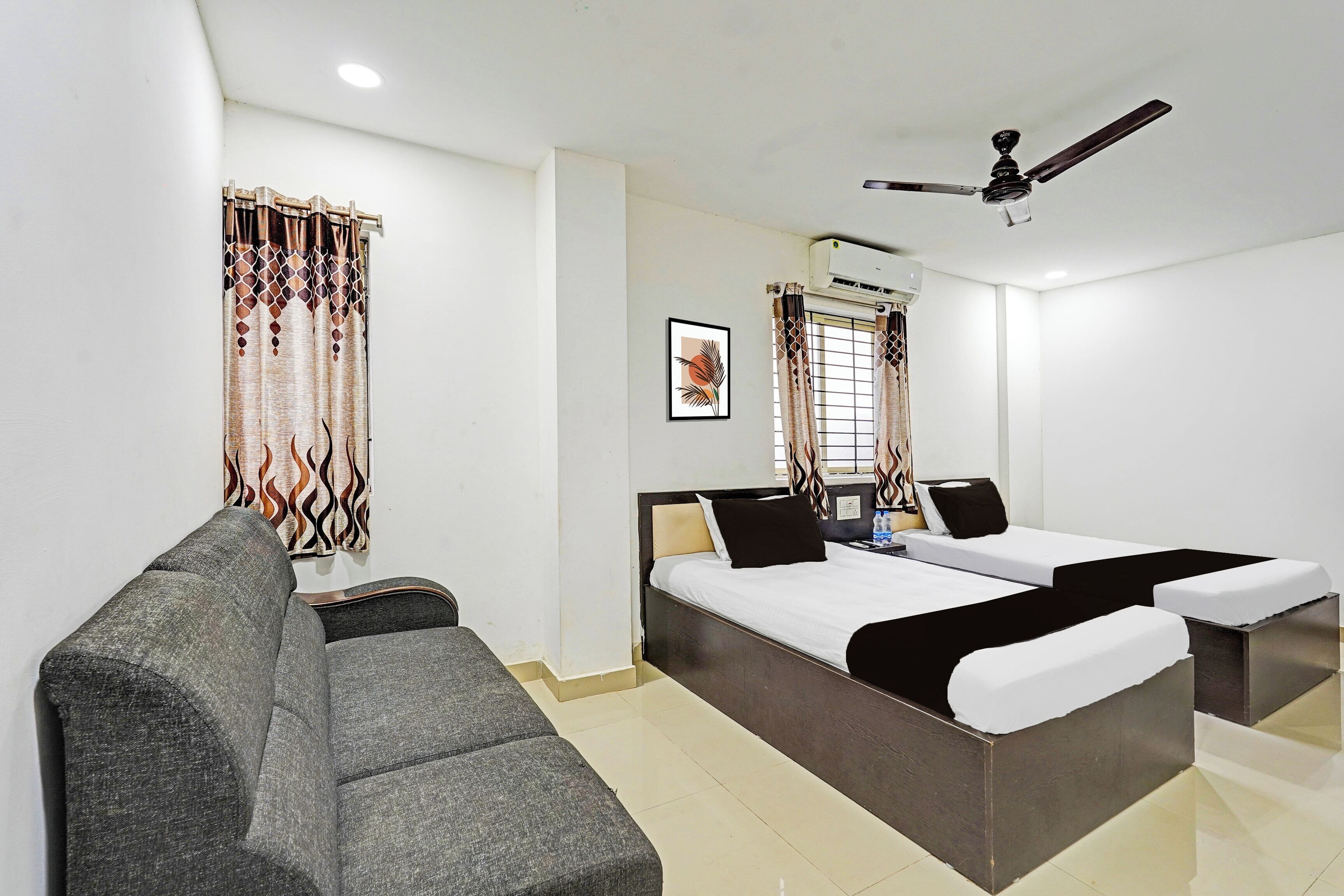 A hotel room with a bed, a sofa, a ceiling fan, and a window with curtains.