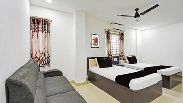 A hotel room with a bed, a sofa, a ceiling fan, and a window with curtains.