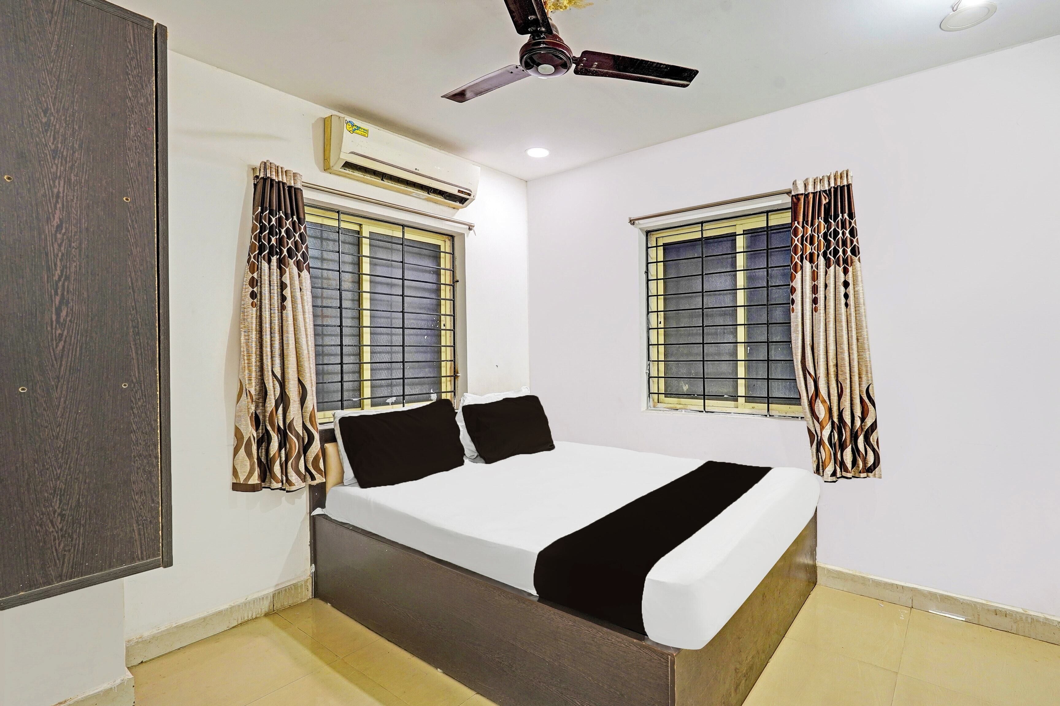 A bedroom with a bed, two windows with curtains, an air conditioning unit, and a ceiling fan.