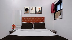 Ein Hotelzimmer mit einem Bett, einem Nachttisch, einer Vase mit Blumen und drei gerahmten Bildern an der Wand.
