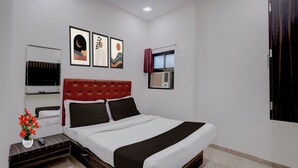 Ein Hotelzimmer mit einem Bett, einem Fernseher, einer Wandklimaanlage und gerahmten Kunstwerken.