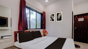 Ein Hotelzimmer mit einem Bett, einem Fernseher, einem Fenster mit Vorhängen, einer Tür und einer Wand mit gerahmten Kunstwerken.