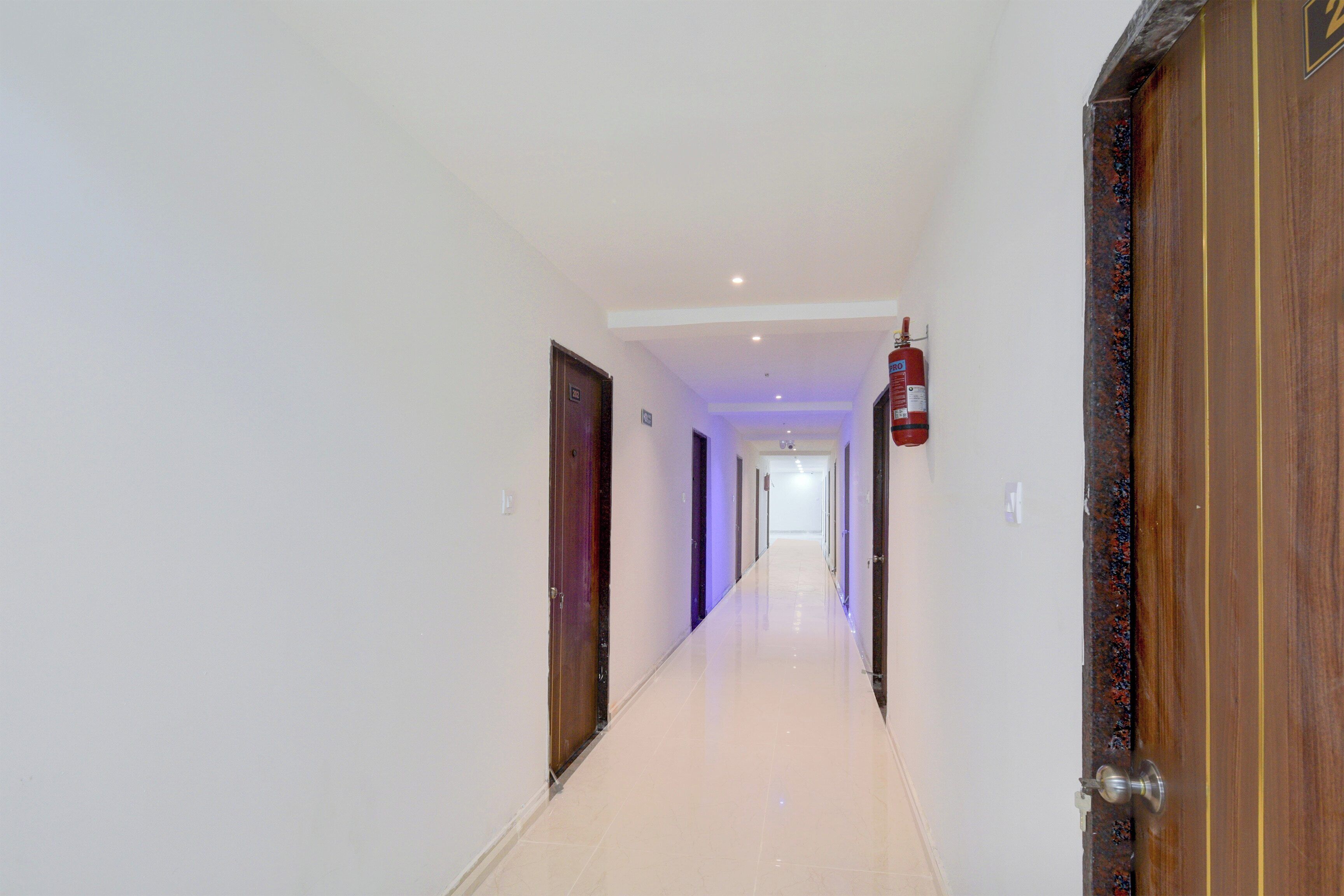 A corridor with doors on both sides, a fire extinguisher mounted on the wall, and a light fixture on the ceiling.