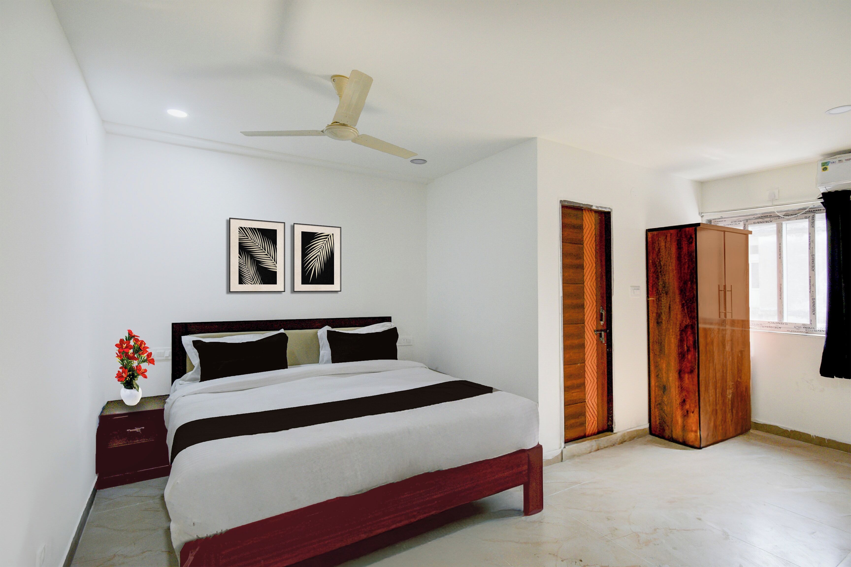 A bedroom with a bed, a nightstand with a vase of flowers, a ceiling fan, and two framed pictures on the wall.