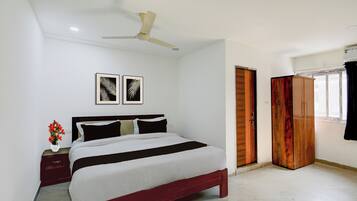 A bedroom with a bed, a nightstand with a vase of flowers, a ceiling fan, and two framed pictures on the wall.