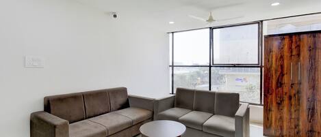 A modern living room with a sectional sofa, a small round table, and a large window offering a view of the city.