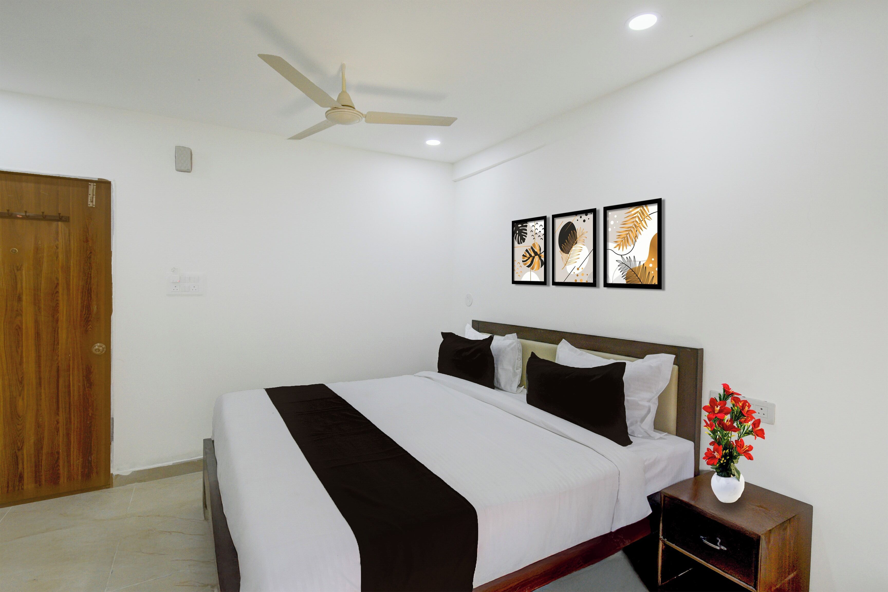 Ein Hotelzimmer mit Bett, Nachttisch, Blumen in einer Vase und Deckenventilator.
