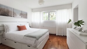 Un dormitorio con cama, mesita de noche, cómoda, ventana con cortinas y una planta.