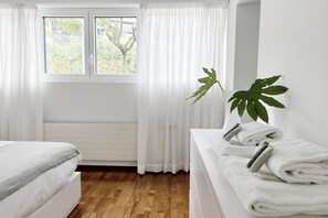Una habitación de hotel con una cama, una mesita de noche con toallas, una ventana con cortinas y una planta.