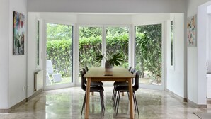 Un comedor con una mesa grande y sillas, ventanas amplias que dan a zonas verdes y obras de arte en las paredes.