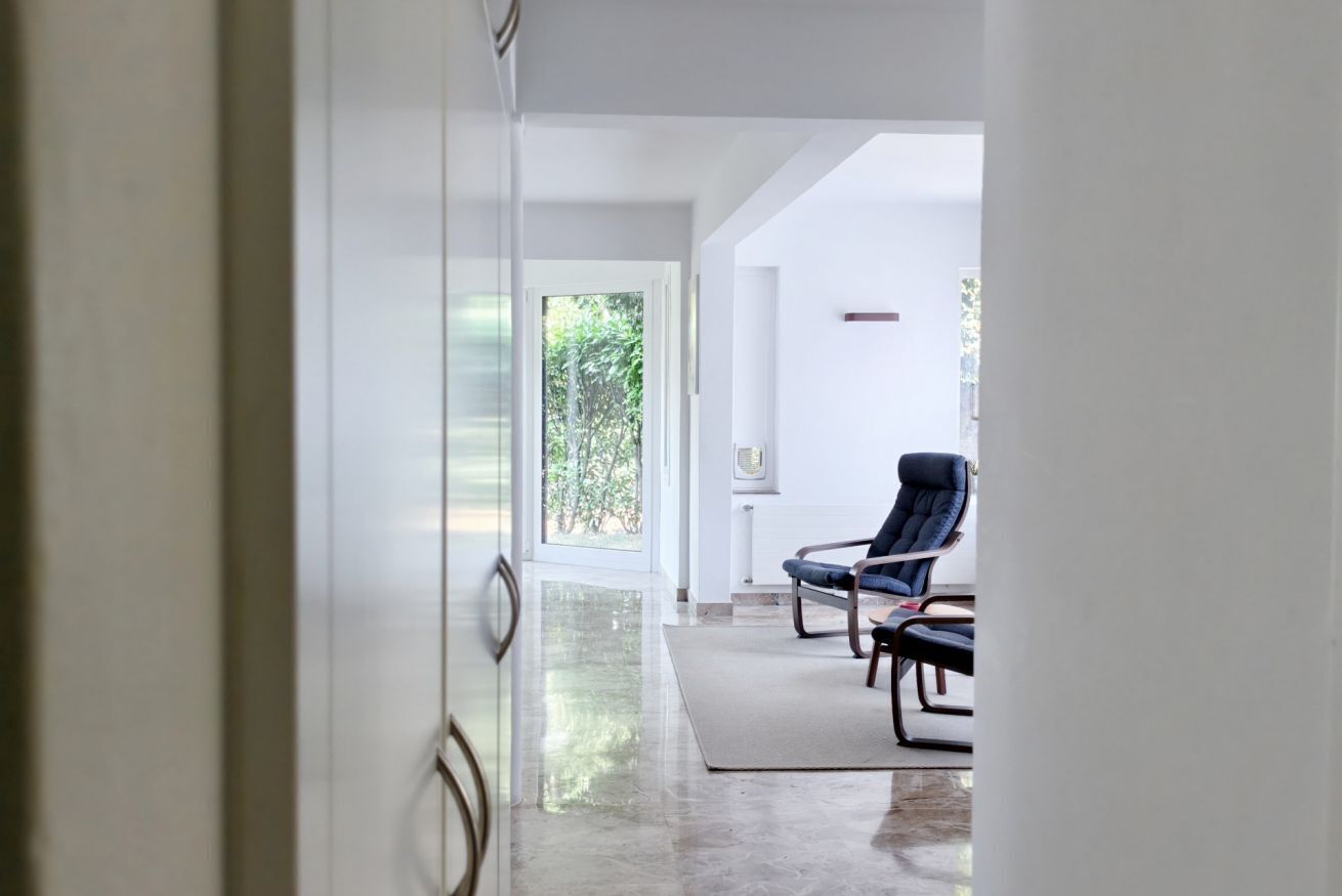A modern interior with a glass door leading to a room with a view of greenery outside. There are two chairs with metal frames and dark upholstery.