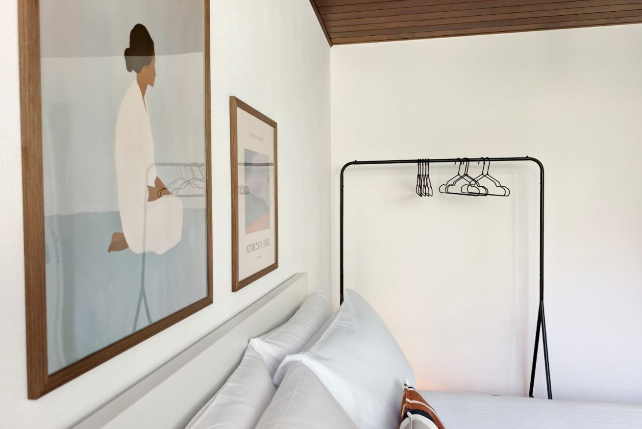 A bedroom with a bed, a wall-mounted clothes rack, and two framed artworks.