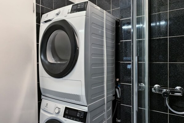 A stacked washer and dryer unit in a bathroom with black tiled walls.