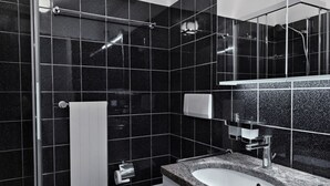 Un baño moderno con pared de azulejos negros, inodoro blanco, lavabo con encimera y zona de ducha.