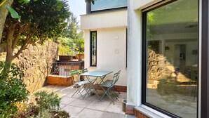 Un patio con una mesa y sillas, un muro de piedra y un amplio ventanal corredera.