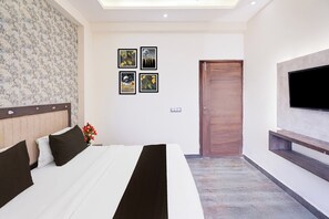 Quarto de hotel com uma cama, televisão na parede e quadros decorativos.