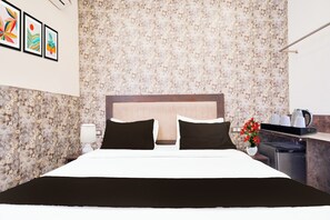 A hotel room with a bed, a nightstand, a lamp, a vase with flowers, and a coffee maker. - Collection O Sector 108 Noida (Noida)