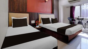 A hotel room with two beds, a red accent wall, an air conditioning unit, a window with curtains, and a small table with a vase of flowers. - Collection O Asalpha Metro Station (Mumbai)