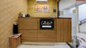 A reception desk with a sign indicating it is company-serviced. There is a framed painting above the desk and a small plant on the left. - Collection O Asalpha Metro Station (Mumbai)