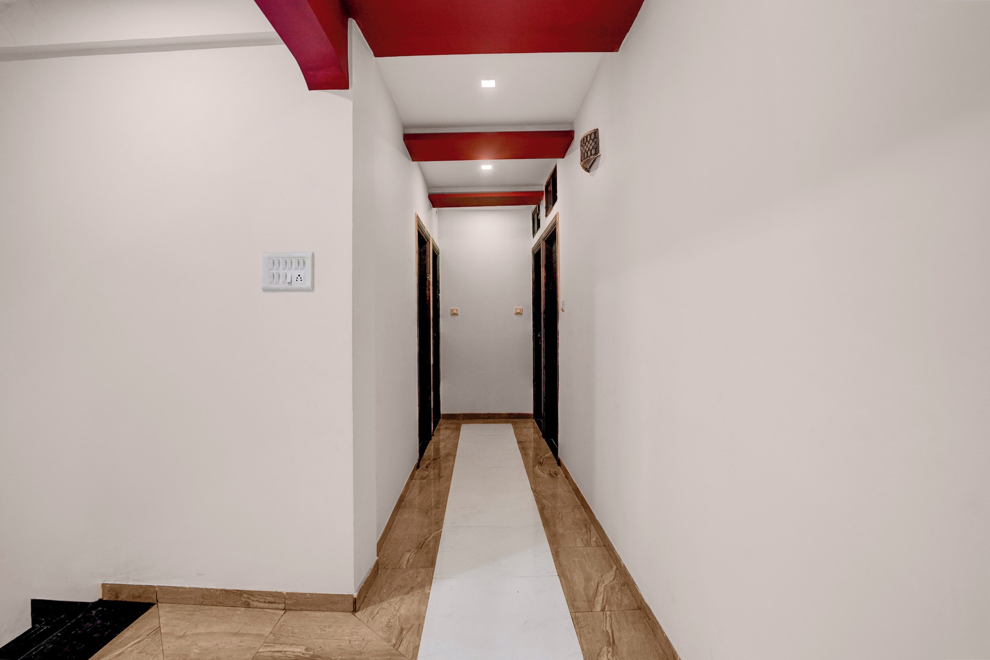 Un pasillo con piso blanco, detalles rojos en el techo e interruptor de luz en la pared.