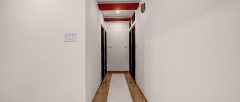 Un pasillo con piso blanco, detalles rojos en el techo e interruptor de luz en la pared.
