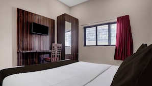 A hotel room with a bed, a TV mounted on a wooden panel wall, a window with curtains, and a wardrobe. - Collection O Asalpha Metro Station (Mumbai)