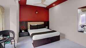 A hotel room with a bed, a chair, a small table, a ceiling fan, and a window. - Collection O Asalpha Metro Station (Mumbai)