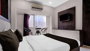 A hotel room with a large bed, a TV mounted on the wall, and a small table with chairs. - Collection O Asalpha Metro Station (Mumbai)