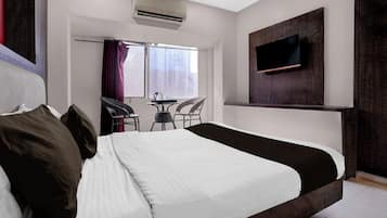 A hotel room with a large bed, a TV mounted on the wall, and a small table with chairs.