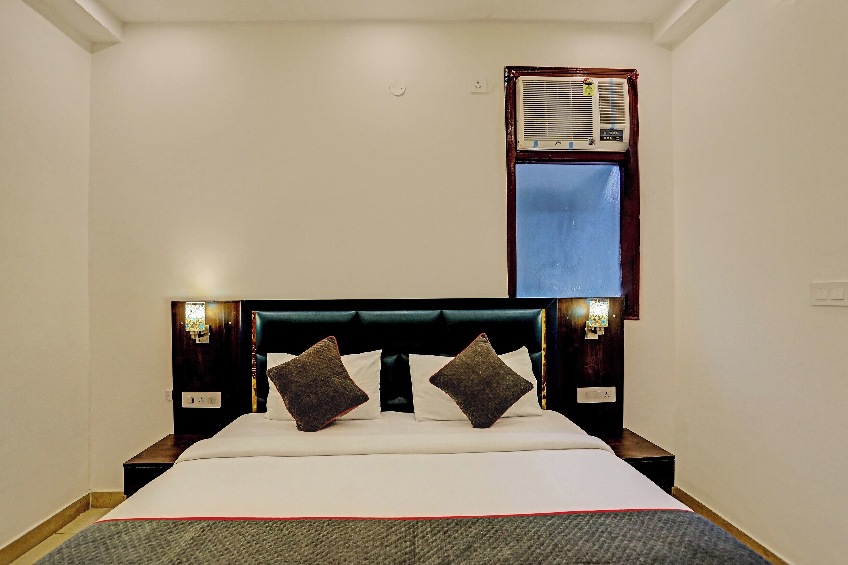 Quarto de hotel com uma cama, duas luminárias de cabeceira, um aparelho de ar condicionado e uma janela.