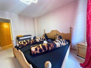 Ein Schlafzimmer mit einem hölzernen Bett, einem Nachttisch, einem Schreibtisch und einem roten Vorhang.
