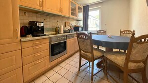 A kitchen with wooden cabinets, a stove, a microwave, and a dining table with chairs. - Spacious Apartment With Balcony (Boppard)