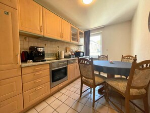 A kitchen with wooden cabinets, a stove, a microwave, and a dining table with chairs.