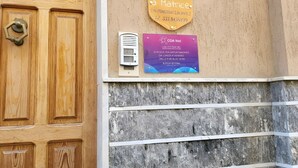 En trædør med en messinggreb, et intercom monteret på væggen, og to skilte: et for et ledigt hus med navnet 'Casa Vacanze Matrice' og kontaktoplysninger, samt et til 'CDA Net' med åbningstider.
