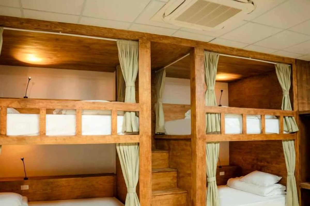 A room with two bunk beds, each with a curtain, a bedside table, and a lamp.