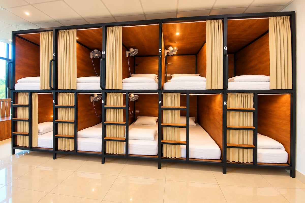 A bunk bed room with wooden walls and curtains, each bed with a pillow and a bedside table.