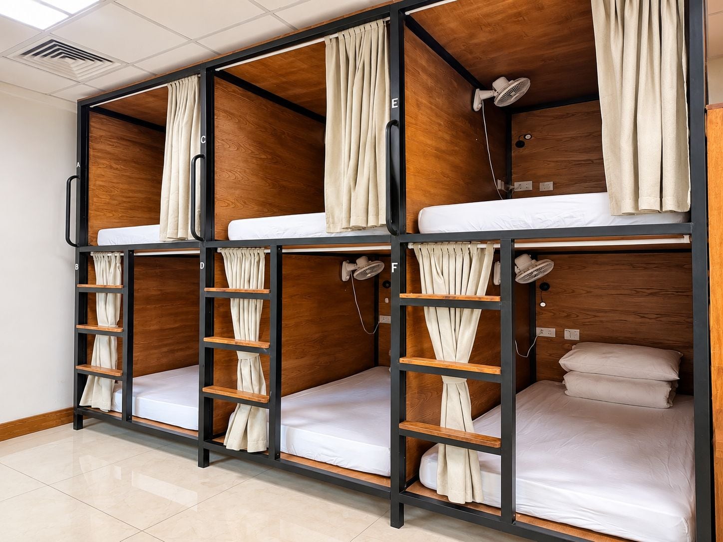 Habitació amb lliteres, cortines, ventilador i escala.