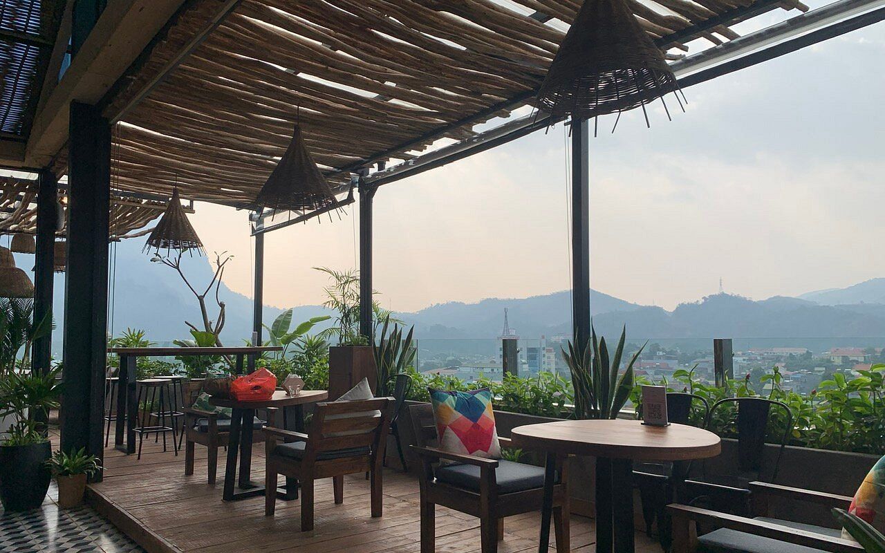 An outdoor seating area with tables and chairs, surrounded by potted plants and a view of distant mountains.
