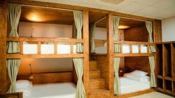 Een kamer met stapelbedden, houten hoofdeinden en gordijnen.