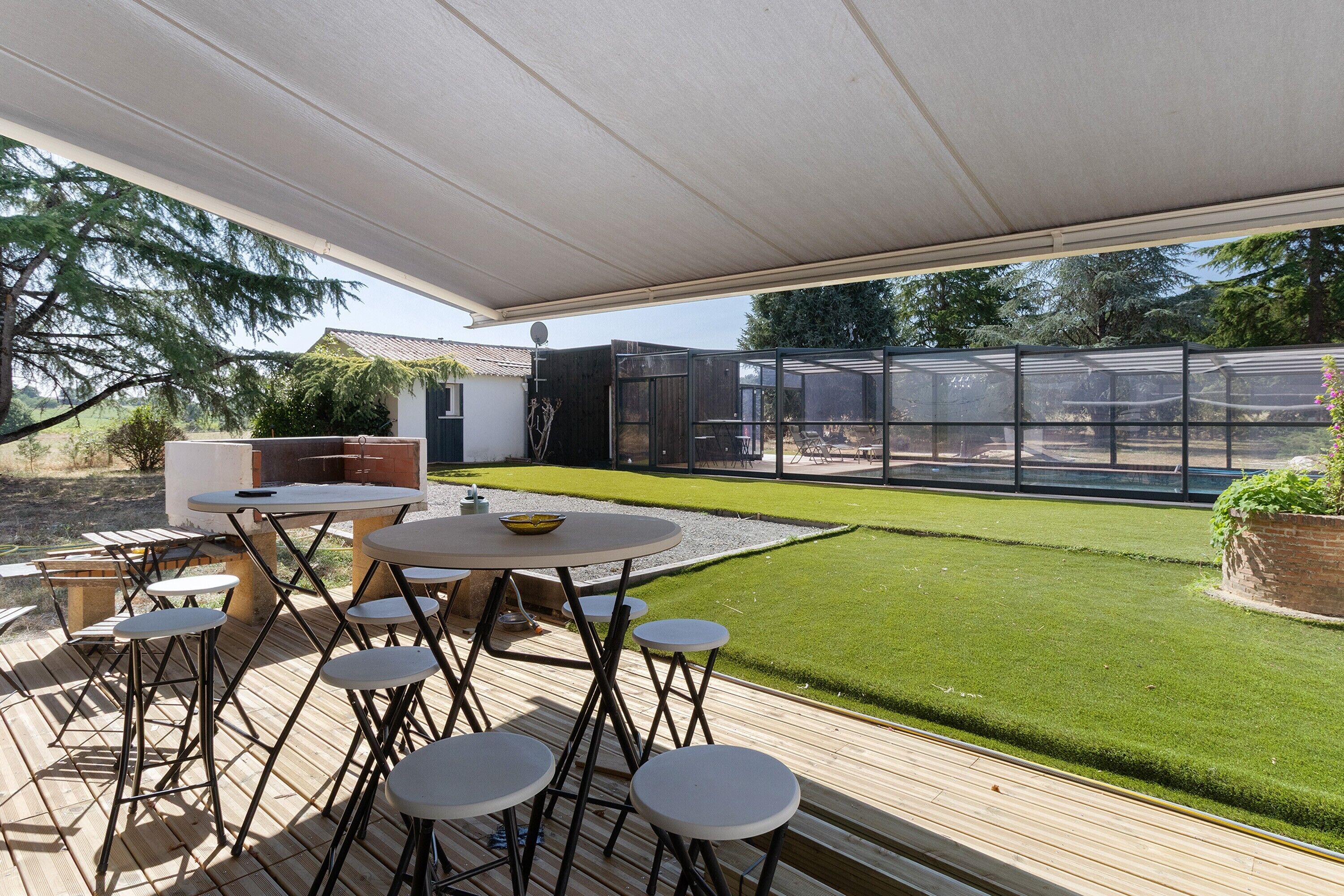An outdoor patio with a table and chairs, a barbecue grill, and a glass enclosure.