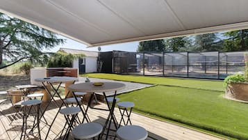 An outdoor patio with a table and chairs, a barbecue grill, and a glass enclosure.