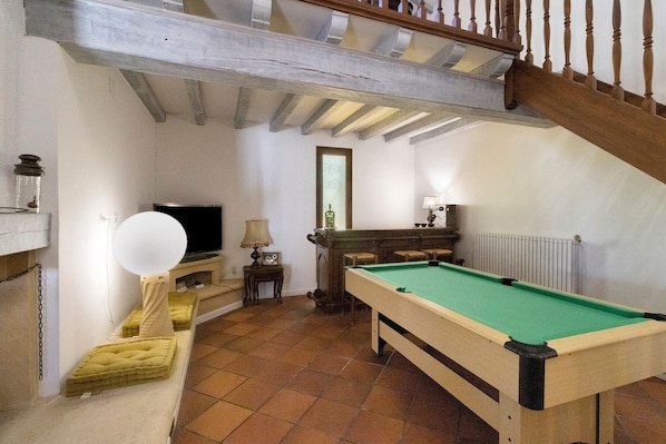 A room with a pool table, a television, and a staircase.