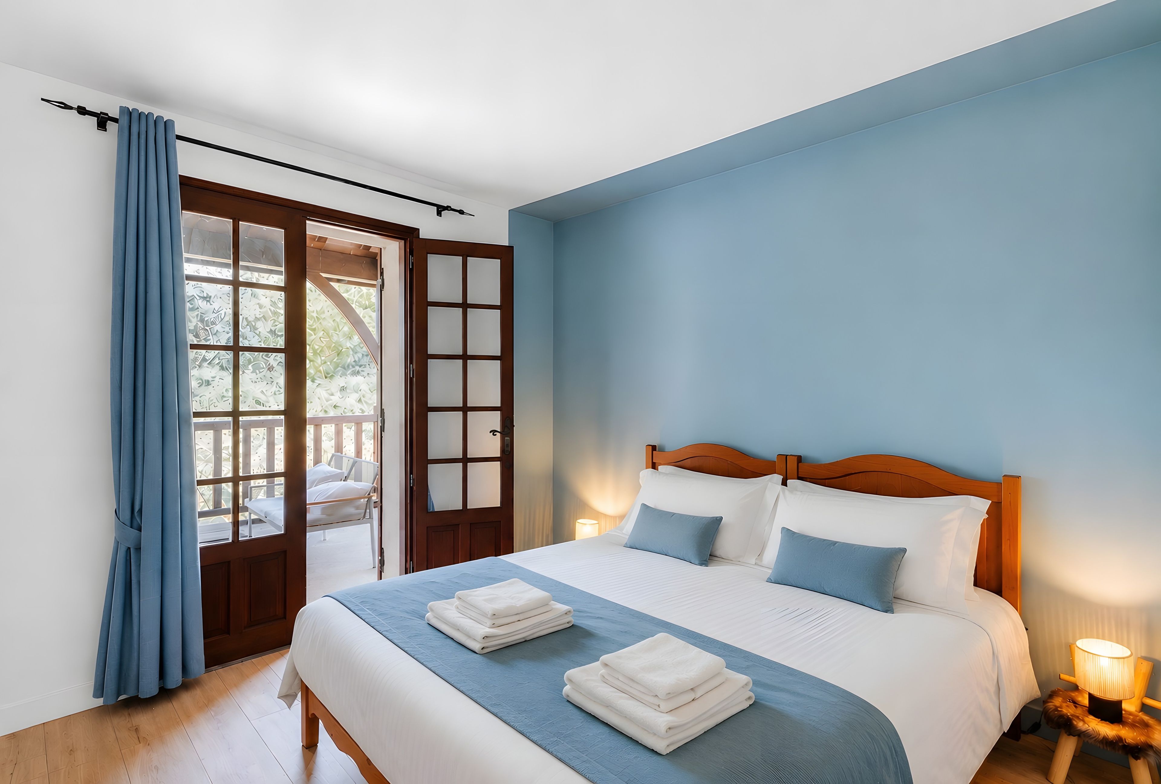 Une chambre à coucher comprenant un lit, une table de chevet, une lampe, une fenêtre avec des rideaux et une porte donnant sur un espace extérieur.