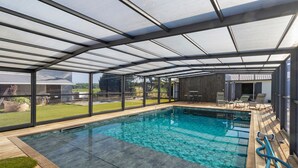 Una piscina techada con agua cristalina, rodeada de una terraza de madera y sillas de descanso.