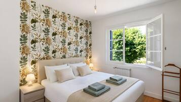 Een slaapkamer met een bed, nachtkastjes, een raam met uitzicht op groen en een radiator.