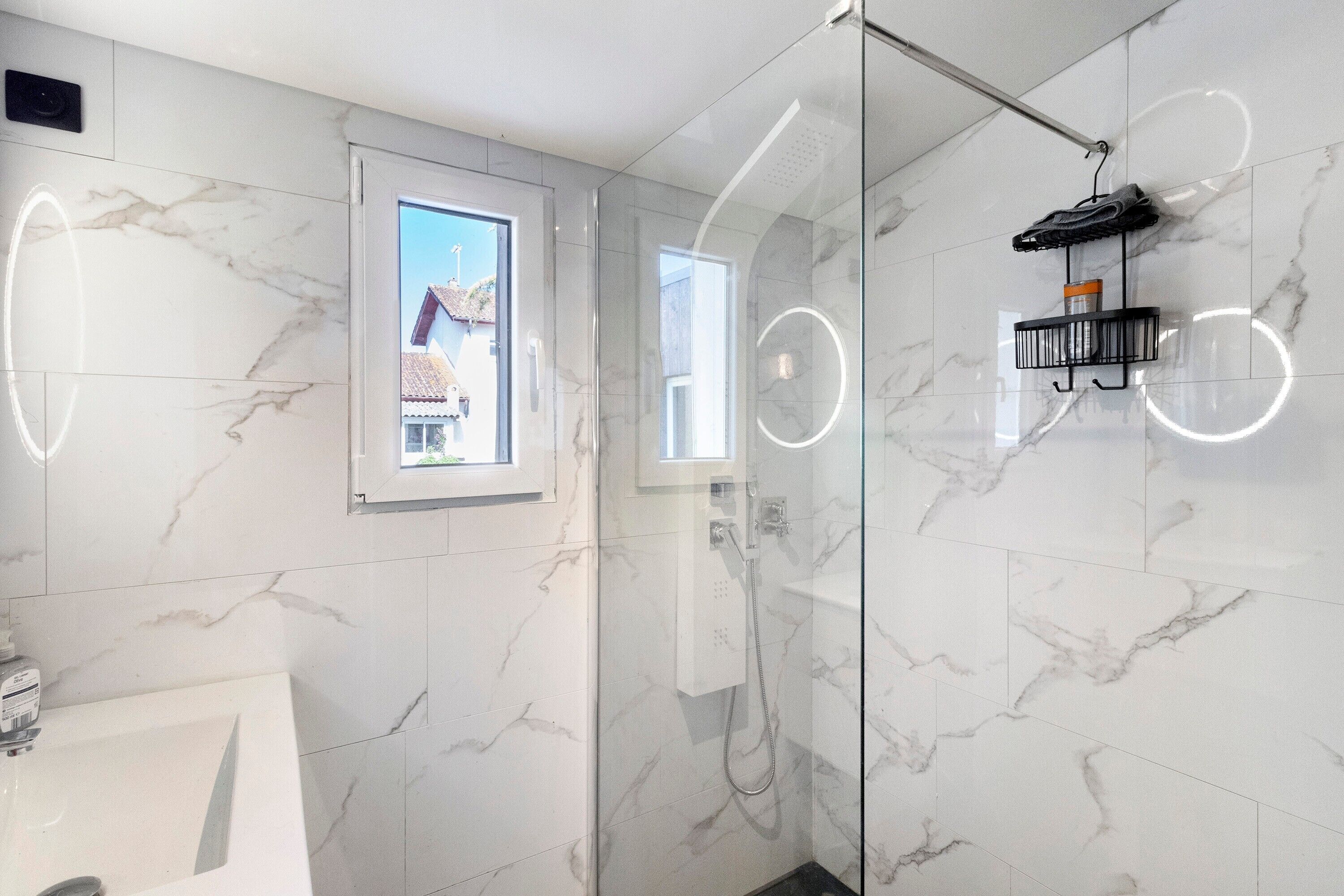 Ein modernes Badezimmer mit Duschkabine aus Glas, einem kleinen Fenster und einem Handtuchhalter.