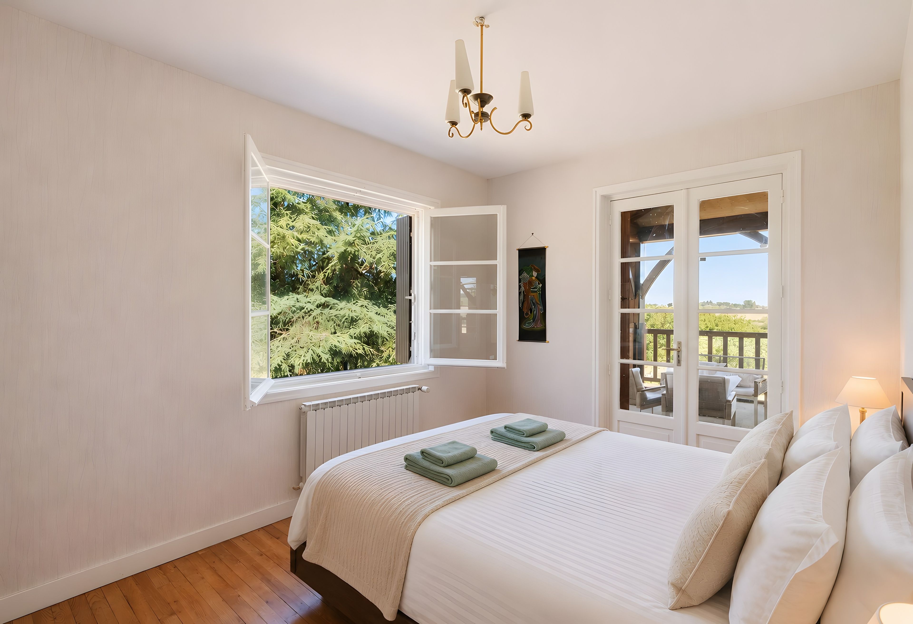 Ein Schlafzimmer mit einem großen Bett, einem Fenster mit Blick auf Grünflächen, einer Kristallleuchter und einer Tür zu einem Außenbereich.