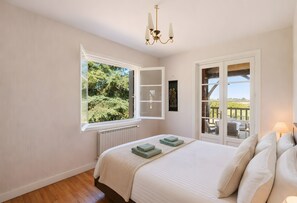 Un dormitorio con una cama grande, una ventana con vistas a zonas verdes, una araña y una puerta que da a un espacio exterior.