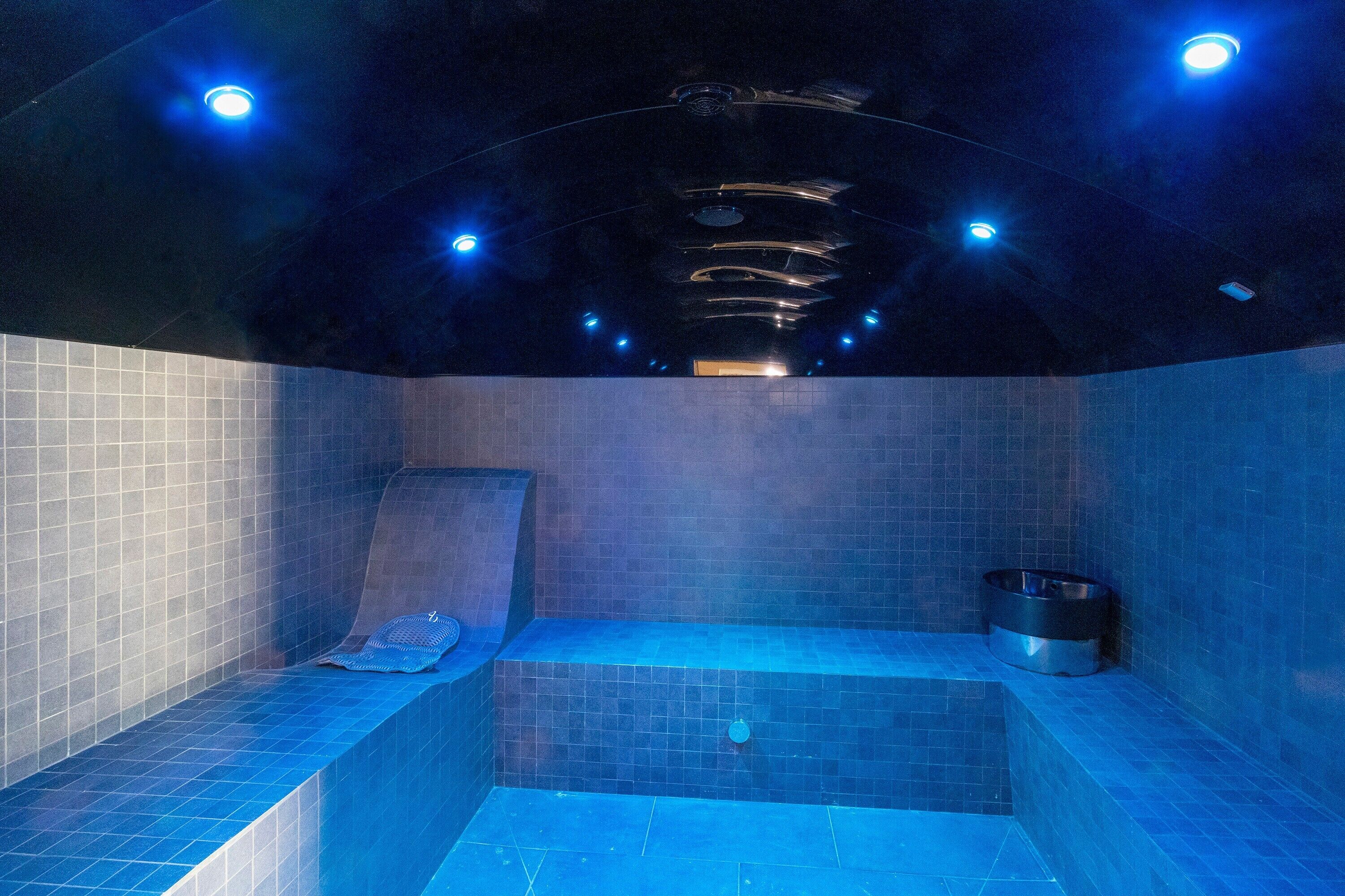 Une salle de spa équipée d’un jacuzzi, de murs carrelés et de luminaires au plafond.